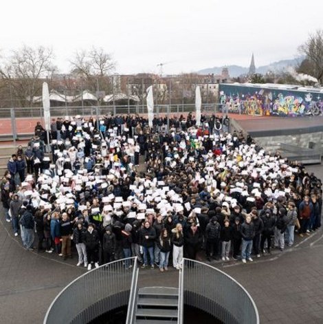 Schulgemeinschaft stellt sich im Schulhof in Form eines Peace-Zeichens auf